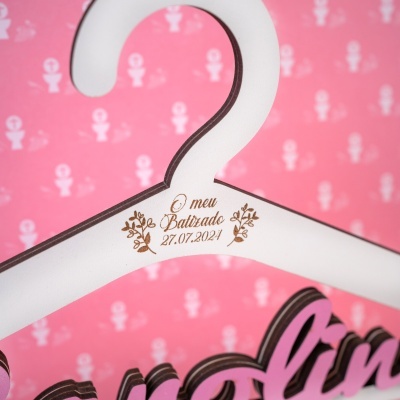 Cabide branco de madeira com gravação O meu Batizado 27.07.2024 e fundo rosa com símbolos religiosos