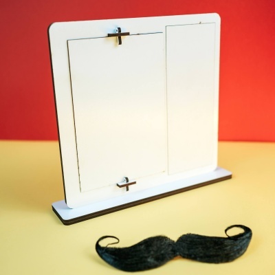 Expositor branco em madeira para duas fotografias sobre mesa amarela com fundo vermelho e bigode preto em primeiro plano