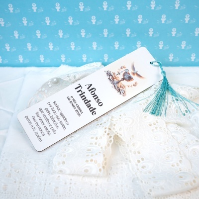 Marcador de papel branco com cordão azul e texto religioso sobre pano rendado branco
