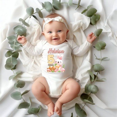 Bebé com body branco estampado e faixa de cabeça branca com laço, sobre tecido branco com folhas verdes ao redor