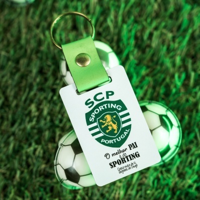 Chaveiro com emblema do Sporting e texto em português em fundo relvado