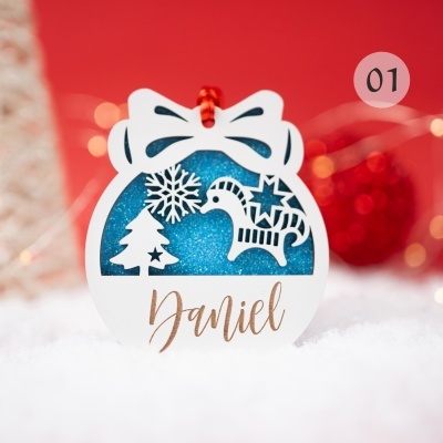 Enfeite natalício branco com nome Daniel sobre fundo vermelho e neve artificial.