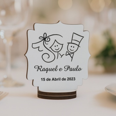 Placa de mesa em madeira com desenho de noivo e noiva e texto com nomes e data