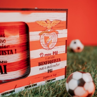 Caixa de madeira vermelha e branca com brasão e texto em português, bola de futebol desfocada em primeiro plano.