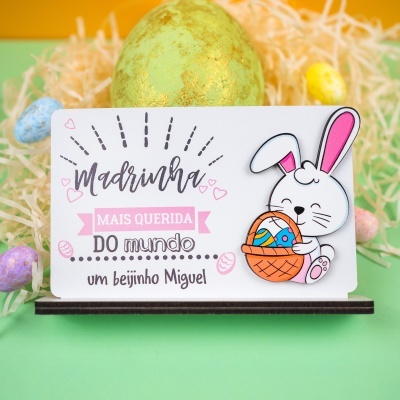 Cartão de papel com texto em português e ilustração de coelho e ovos de Páscoa coloridos.
