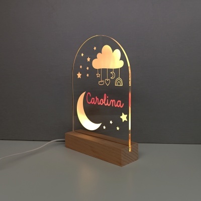 Luminária com base em madeira e painel acrílico iluminado com desenhos de nuvem e estrelas.