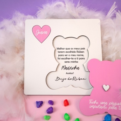 Cartão convite para madrinha com texto, coração rosa e pedras coloridas numa superfície cor-de-rosa