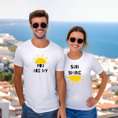 Casal com t-shirts brancas e óculos de sol junto a uma paisagem costeira