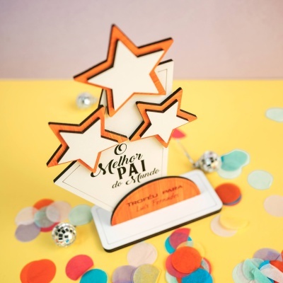 Placa de madeira decorativa com estrelas e texto em português rodeada de confetes coloridos