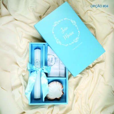 Caixa azul personalizada com vela, lenço e concha sobre tecido creme