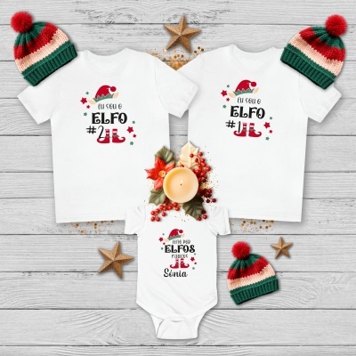 Três peças de roupa branca com textos festivos e gorros de malha tricolor em ambiente natalício