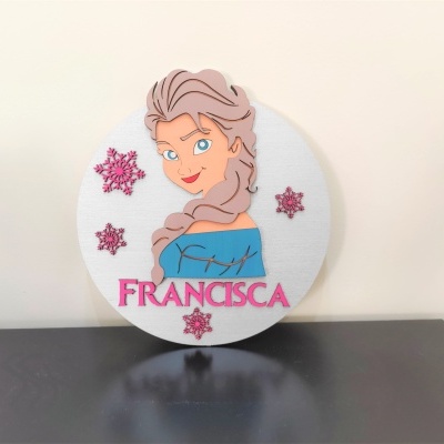 Decoração redonda em madeira com relevo da personagem Elsa, flocos de neve cor de rosa e o nome FRANCISCA.