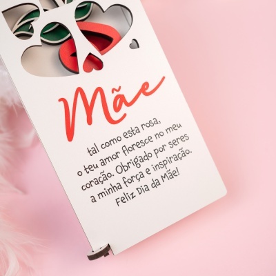 Cartão branco com recortes de corações e texto para o Dia da Mãe sobre fundo rosa.