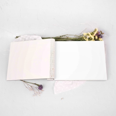 Livro aberto com páginas brancas sobre tecido branco e flores secas amarelas e roxas
