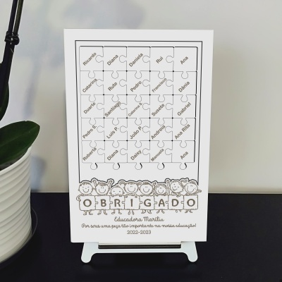 Quadro branco com peças de puzzle e nomes, com a palavra OBRIGADO e ilustrações de crianças na base.
