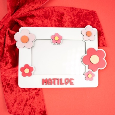 Moldura branca decorada com flores vermelhas e rosa e texto MATILDE sobre fundo vermelho com fita de veludo