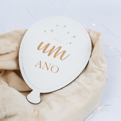 Placa decorativa branca em formato de balão com texto dourado um ANO