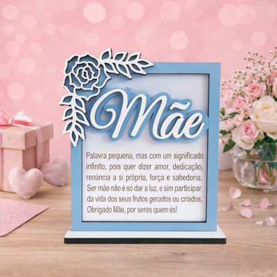 Placa decorativa azul e branca com texto sobre Mãe e flores, presente rosa e vaso com flores em fundo rosa.