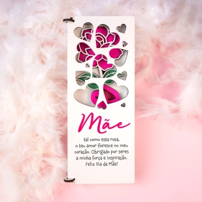 Cartão Dia da Mãe branco com recortes de corações e rosa, texto em português, sobre fundo de penas cor de rosa.
