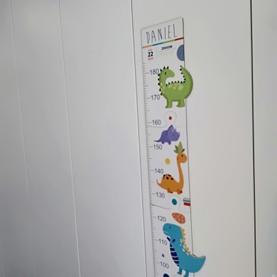 Régua de medição infantil com dinossauros coloridos e nome Daniel na parede