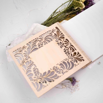 Livro com capa madeira clara recortada, páginas brancas, flores secas e tecido branco