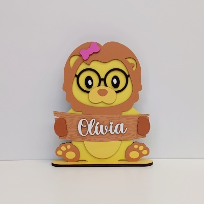 Produto decorativo de madeira com urso amarelo e castanho segurando uma placa com o nome Olívia