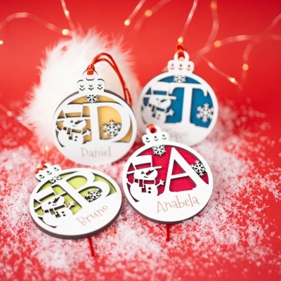 Bolas decorativas de Natal personalizadas com nomes sobre fundo vermelho e neve artificial.