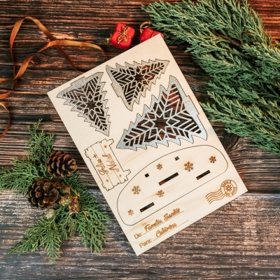 Placa de madeira com recortes para árvore de Natal, texto gravado em português, pinhas e ramos verdes numa mesa de madeira