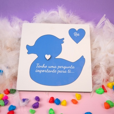 Placa com pato azul e texto em português rodeada por penas brancas e pedras coloridas