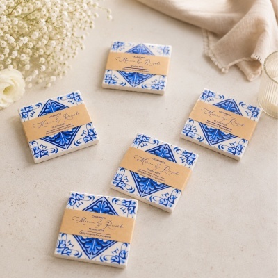 Azulejos em padrão azul e branco com faixas de papel bege, texto de casamento, flores e tecido ao fundo