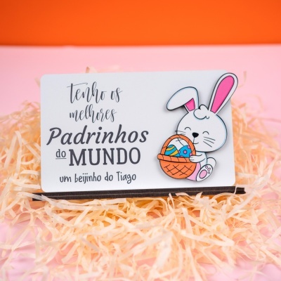 Cartão com texto e desenho de coelho com cesta de ovos coloridos sobre fundo cor-de-rosa e laranja.