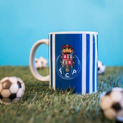 Caneca com riscas azuis e emblema FCP sobre relva com bolas de futebol