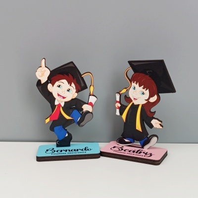 Ornamentos de parabéns para finalistas com figuras de menino e menina a usar beca e capelo e bases com nomes e datas.