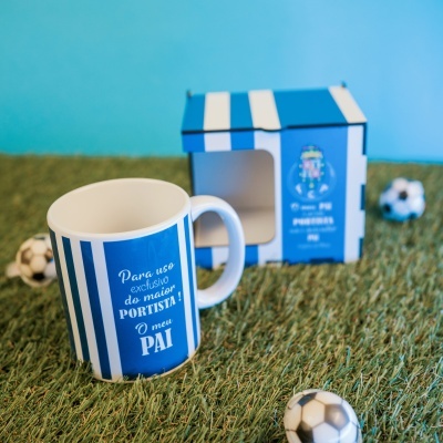 Caneca branca e azul com texto em português e mini bolas de futebol sobre relva sintética