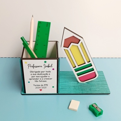 Organizador de secretária com canetas, régua e apontador verdes, lápis bege, borracha branca, decoração de lápis colorido e etiqueta com texto para professora.