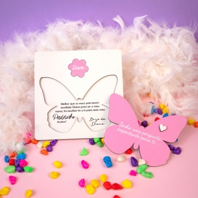 Convite borboleta branco com selo rosa e pedras coloridas sobre fundo rosa com penas brancas