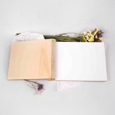 Livro aberto com capa de madeira, páginas em branco e flores secas ao lado