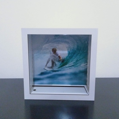 Fotografia de uma pessoa a surfar uma onda azul emoldurada a branco