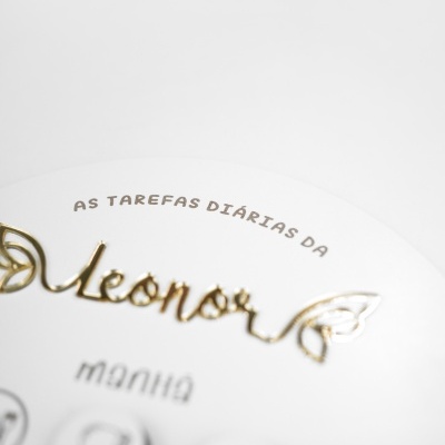 Placa redonda branca com texto dourado e preto, detalhes dourados e ícones circulares.