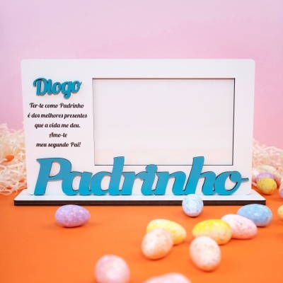Moldura fotográfica com mensagem para padrinho em azul e preto sobre fundo rosa e mesa laranja com ovos coloridos.