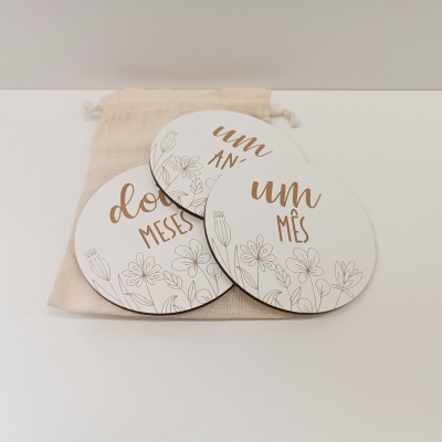 Conjunto de placas redondas brancas com flores douradas e texto sobre bolsa de tecido