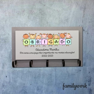 Quadro de madeira cinza com ilustração de crianças coloridas e palavra OBRIGADO formada por peças de puzzle e texto de agradecimento.
