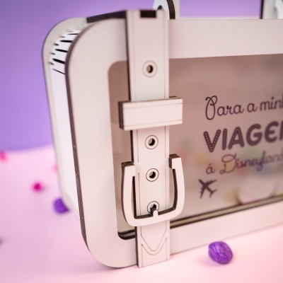 Mala branca com fecho em formato de torre, texto em português e fundo rosa com pedras.