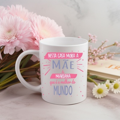 Caneca branca com texto em rosa e azul e flores naturais rosa e brancas ao fundo