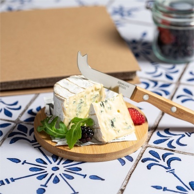 Queijo cremoso branco com bolor azul num prato de madeira com frutas e folha verde e faca de aço inox