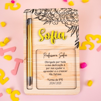 Prenda em madeira clara personalizada com caneta dourada e texto de agradecimento para professora Sofia sobre fundo rosa