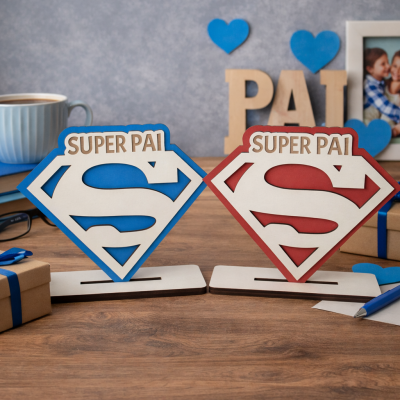 Dois suportes decorativos em madeira com o símbolo do Superman e a frase SUPER PAI, um azul e outro vermelho, sobre mesa de madeira com objetos em redor.