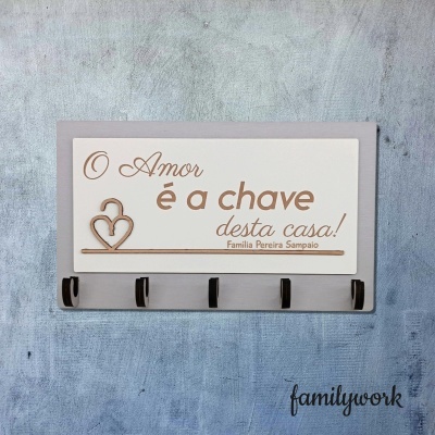 Cabideiro de parede com cinco ganchos e placa decorativa com texto sobre amor e chave da casa em português.