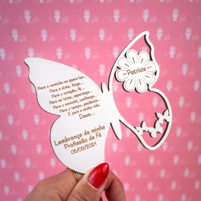 Cartão em forma de borboleta com texto e nome Patrícia, fundo rosa com padrão branco, mão com unha vermelha segurando o cartão.