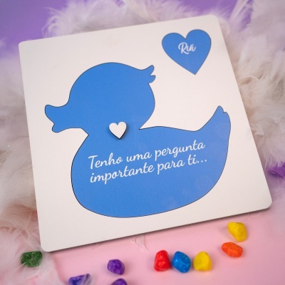 Cartão com pato azul e texto em português sobre fundo lilás e rosa com penas e pedras coloridas